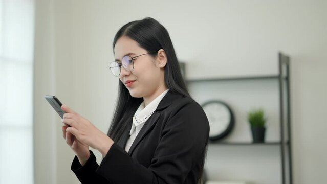 Smart asian woman business wearing glasses and black suit live in office, She use her mobile phone to chatting and looking for someone on footbridge. Slow Motion Shot. 