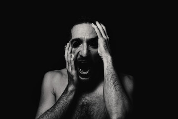 Male portrait in horror style. Black-white male portrait on a black background. Man grabs his face...