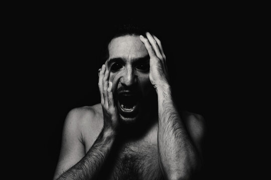 Male portrait in horror style. Black-white male portrait on a black background. Man grabs his face in madness