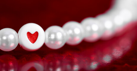  Pearl beads with a heart shaped pendant on a red background. Festive card for Valentines Day, soft focus