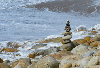 Cairn de galets en équilibre attaqué par les vagues de la marée montante.