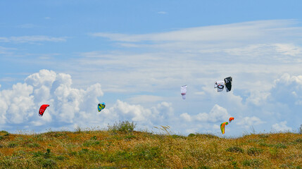 Ensemble d'ailes de kite surf colorées sur fond de ciel nuageux surplombant la dune verdoyante.