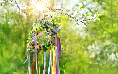 Spring flower wreath with colorful ribbons in garden, green natural background. floral decor. Symbol of Beltane, Wiccan Celtic Holiday beginning of summer. pagan witch traditions and rituals - obrazy, fototapety, plakaty
