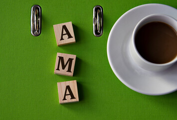AMA - acronym on wooden cubes against the background of a green folder and a cup of coffee