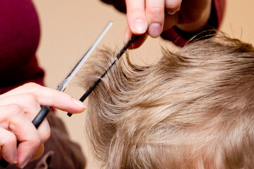 Hairdressing saloon at home in quarantine conditions. Mother cuts boy's hair with scissors.