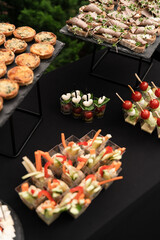 wedding catering on a green lawn. the tables are covered with a black tablecloth and various snacks and fruits and desserts