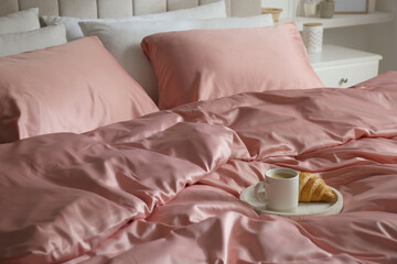 Croissant and coffee in breakfast tray on bed with beautiful pink silk linens indoors - obrazy, fototapety, plakaty