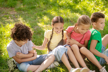 Naklejka na ściany i meble Smiling children sitting on grass in park