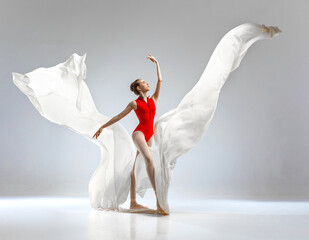 Ballerina in red ballet leotard dancing with white long cloth. She wears ballet pointe shoes. She...