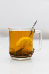 A glass cup of hot tea with honey and lemon on a light background.