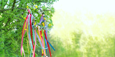 Spring flower wreath with colorful ribbons in garden, green natural background. floral decor, Symbol of Beltane, Wiccan Celtic Holiday beginning of summer. pagan witch traditions, rituals. banner - obrazy, fototapety, plakaty