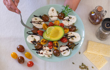 Fresh inviting caprese salad. Female hands hold a plate with cheese mozzarella and small tomatoes, pepper and balsamic. Half avocado to complete a healthy Mediterranean meal