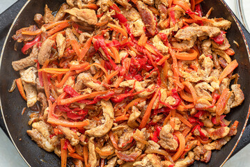 Pork meat is stewed in a pan with peppers, carrots, onions.
