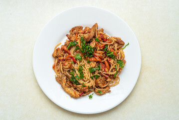 Top view of a plate with rice noodles, pork meat, peppers, carrots, onions.