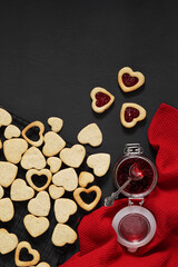 Obraz na płótnie Canvas Linzer cookies filled with jam in heart foarm on a dark table. top view, vertical orientation copy space