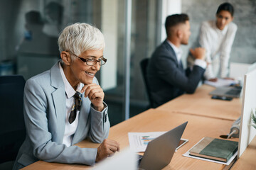 Happy senior businesswoman reads an e-mail on laptop while working in office.