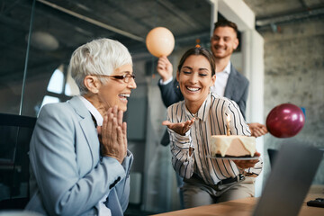 Happy businesswoman and her male colleague surprising their senior CEO with cake for her Birthday in the office.