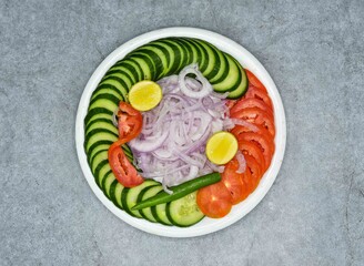 Fresh healthy salad bowl with cucumber, onion, tomato, lemon and green chili on dark grey background top view pakistani salad