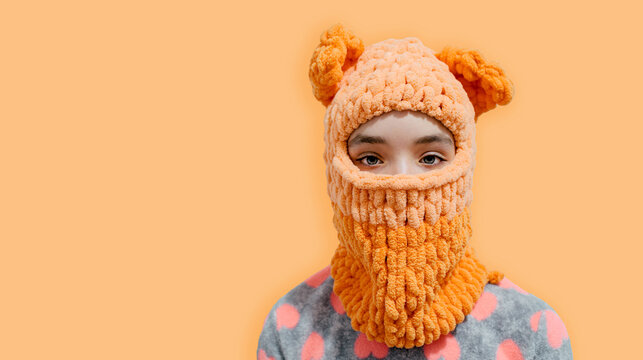 A teenage girl is dressed in a balaclava with bear ears, knitted with her own hands using alize puffy threads. New hat style.