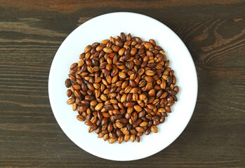 Top View of a Plate of Roasted Barley Kernel for Brewing Barley Tea or Mugicha on Black Wooden Backdrop