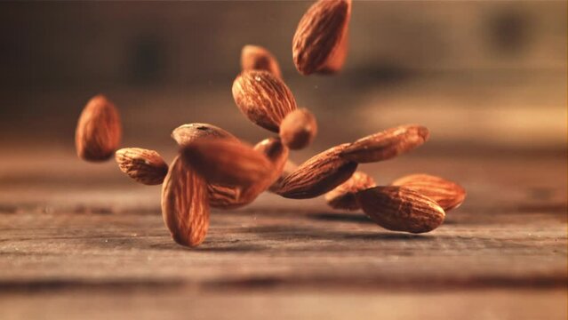 Almonds fall on the table. On a wooden background. Filmed on a high-speed camera at 1000 fps. High quality FullHD footage