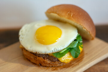 Cheeseburger with open bread, showing fried egg, arugula, cheese and patty.