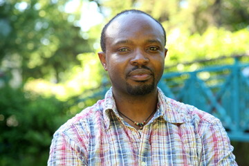 Young african man with outdoor clothes, looking into the camera, outdoor in park, sunny atmosphere