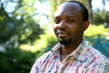 Young african man with outdoor clothes, looking into the camera, outdoor in park, sunny atmosphere