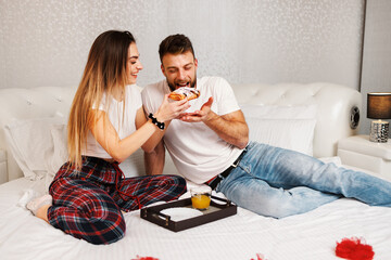 Young couple having breakfast in the bedroom on the bed