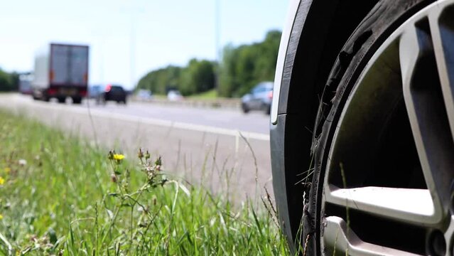A car with a flat tyre after a large blow out on the highway showing a large slit in the tyre at the side of the M25 motorway in London in the UK