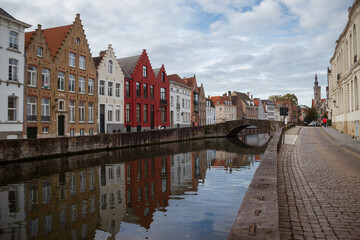 Naklejka premium Imagen de casitas de colores reflejadas en las aguas de los Canales de brujas Belgica con un vuelo azul con nubes y un puente de piedra al fondo haciendo viaje de turismo por europa