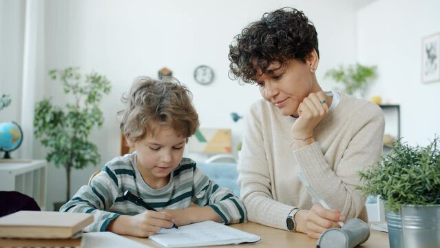 Mother helping child with maths homework writing talking then hugging and kissing child at home. Education and family relationship concept.
