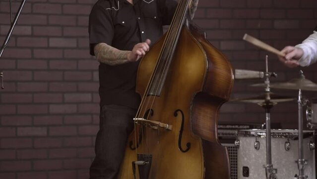 This video shows a close up view of an anonymous musician with tattoos playing a stand up bass instrument on stage.