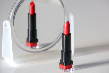 Single opened tube of satin finish red lipstick and make up mirror on the table, studio shot