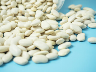 dry white beans scattered from a plastic container on a blue table. copy space
