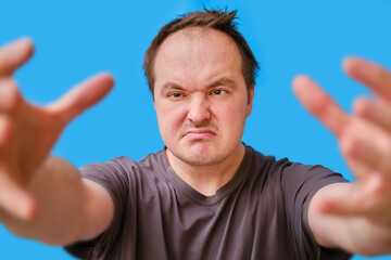 Portrait of a disheveled-looking adult man pulling his arms forward, blue studio background