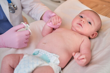 The doctor cuts the nails on the hand of a newborn baby. Nurse in uniform with scissors for child hygiene