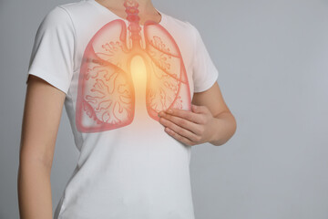 Woman holding hand near chest with illustration of lungs on light grey background, closeup
