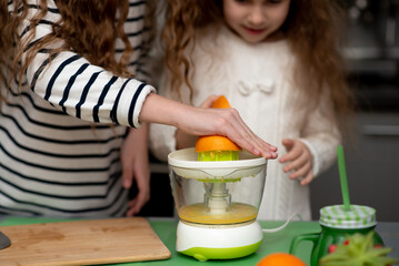 Two cute sister girls are making orange fresh juice.Hands close-up. They are in the kitchen at home. Family. Fresh fruit.