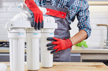 Plumber installs or change water filter. Replacement aqua filter. Repairman installing water filter cartridges in kitchen. Installation of reverse osmosis water purification system. - obrazy, fototapety, plakaty