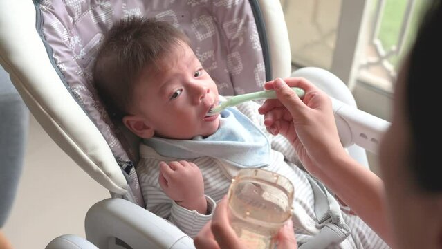 Baby boy being fed water in his high chair at home