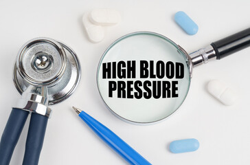 On a white surface lie pills, a pen, a stethoscope and a magnifying glass with the inscription - High blood pressure