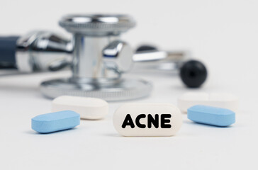 Obraz na płótnie Canvas On a white surface lie pills, a stethoscope and a tablet with the inscription - ACNE