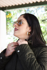 Mujer hispana ajustándose la chaqueta. Mujer Guatemalteca con cabello negro usando lentes de sol y...