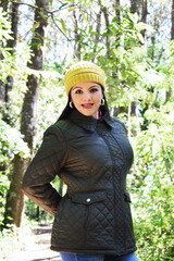Mujer latina modelando una chaqueta verde obscuro, jeans azules y gorro amarillo. Mujer...