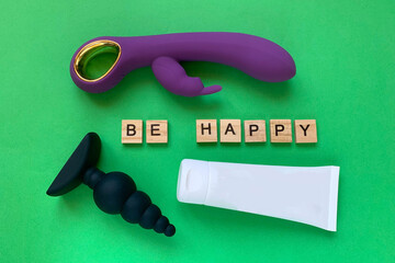 Sex toys and lubricant. Vibrator, butt plug and tube on green background. Letter BE HAPPY. Useful...