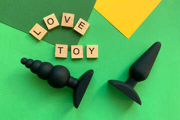 Sex toys. Two black butt plags on green background. Lettering LOVE TOY. Useful for adult, sex shop