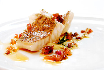 sea bass fillet with skin in olive oil and tomato and spices on a plate on a white background, close up view - obrazy, fototapety, plakaty