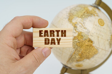 A man holds in his hand a wooden plate on which it is written - Earth Day. In the background is a globe.