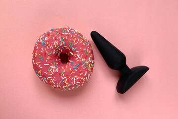 Sex toy. Black butt plag and donut on a pink background. Useful for adult, sex shop